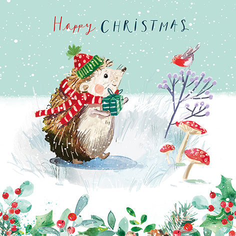 Christmas card design showing a happy hedgehog waking through snow to deliver a present, text reads 'Happy Christmas'.