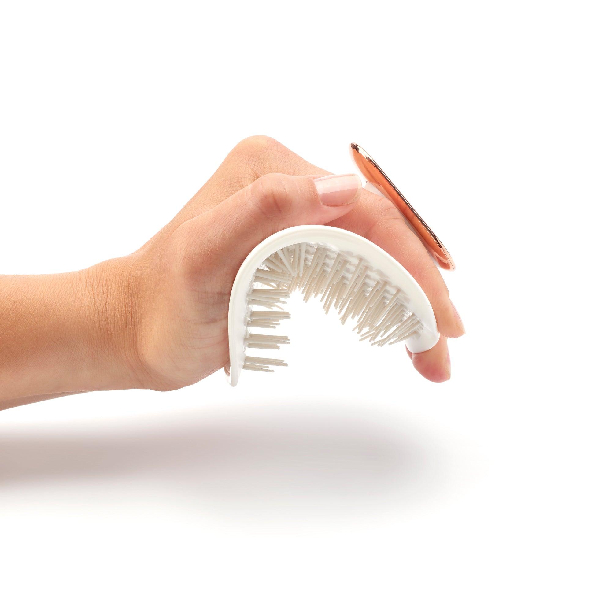 MANTA brush with a non-slip handle in white and rose gold, being flexed in the palm of the hand. 