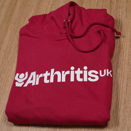 Folded raspberry pink hoodie with 'Arthritis UK' text on a wooden surface