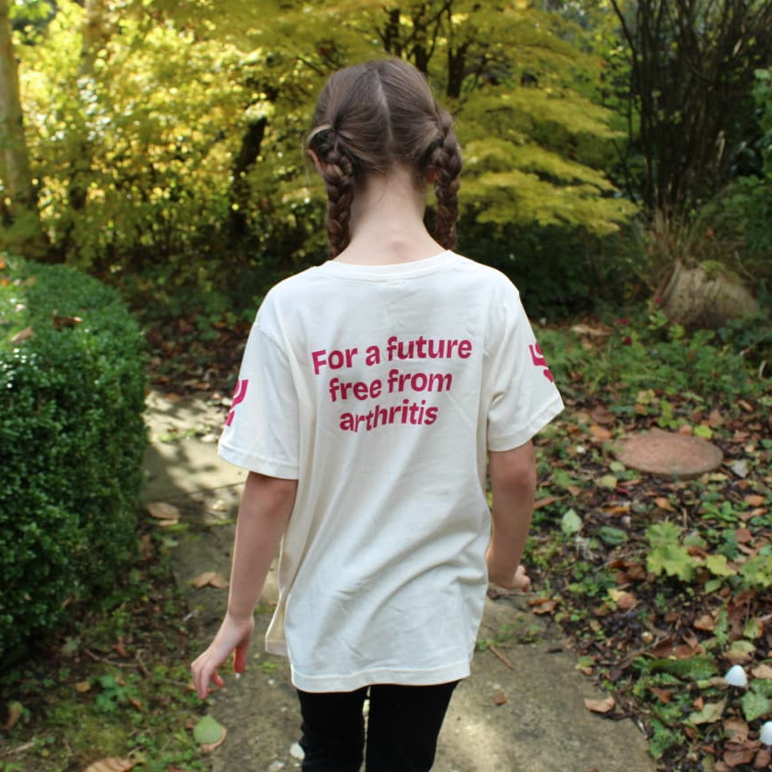 Person wearing a white t-shirt with text 'For a future free from arthritis' in a garden setting.
