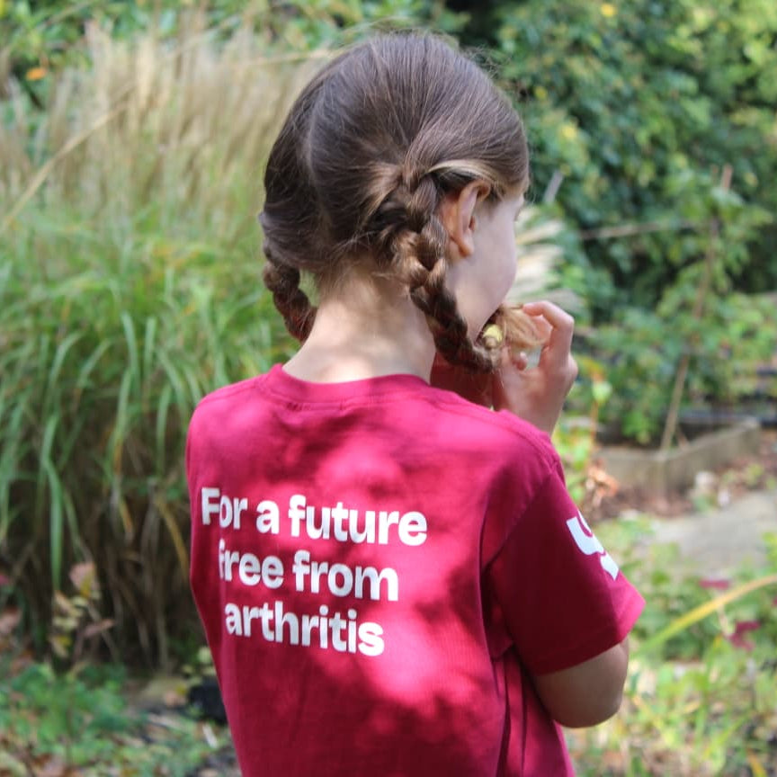 Person wearing a red shirt with text 'For a future free from arthritis' in an outdoor setting.
