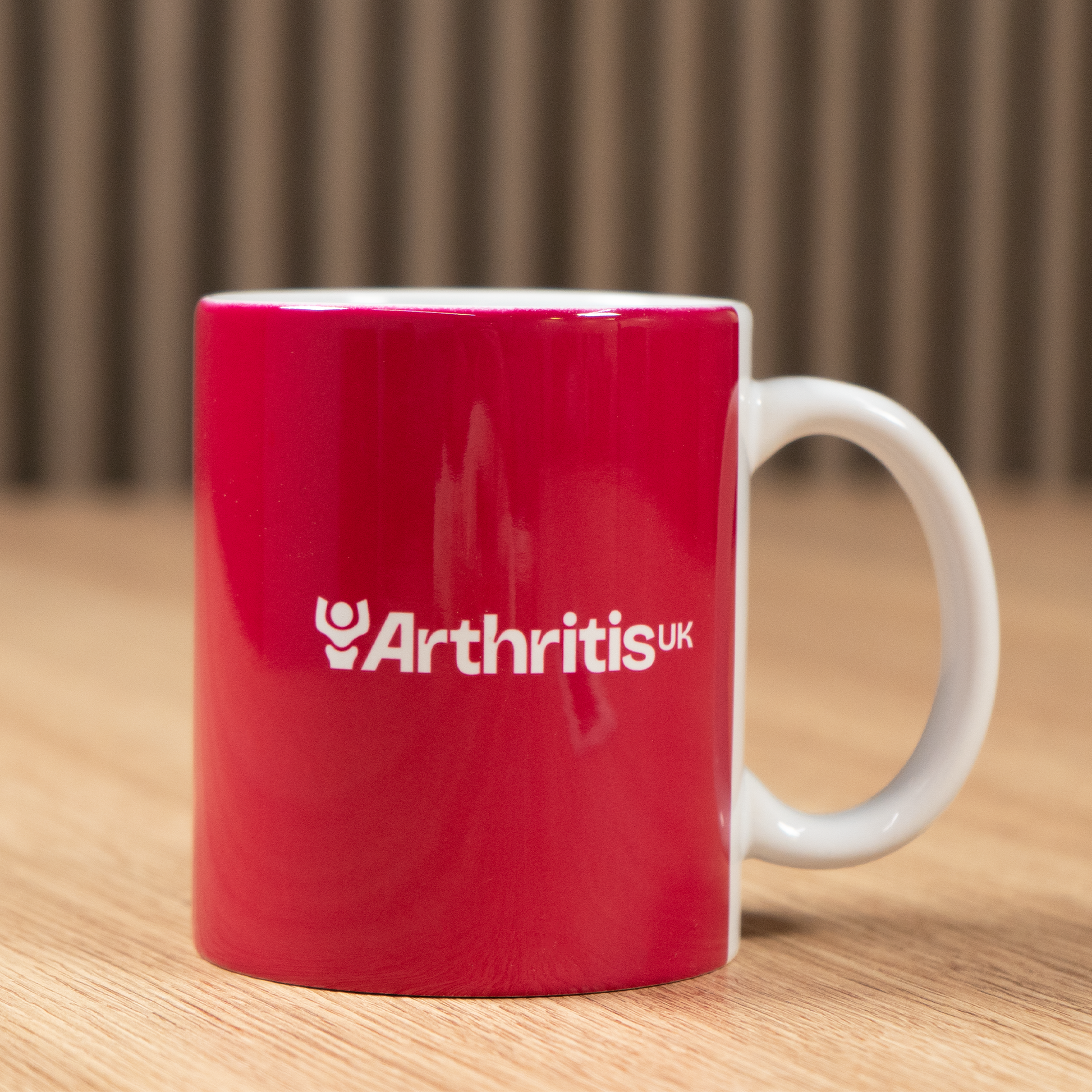Raspberry mug with 'Arthritis UK' logo on a wooden surface