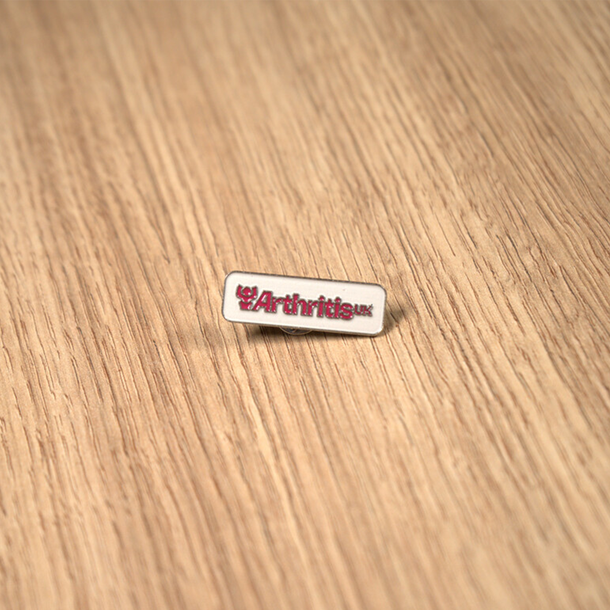 White and raspberry pin with 'Arthritis UK' logo on a wooden surface