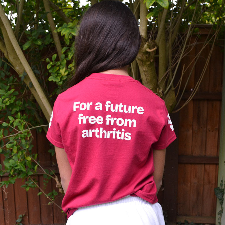 Person wearing a raspberry Arthritis UK  t-shirt with text 'For a future free from arthritis' outdoors.