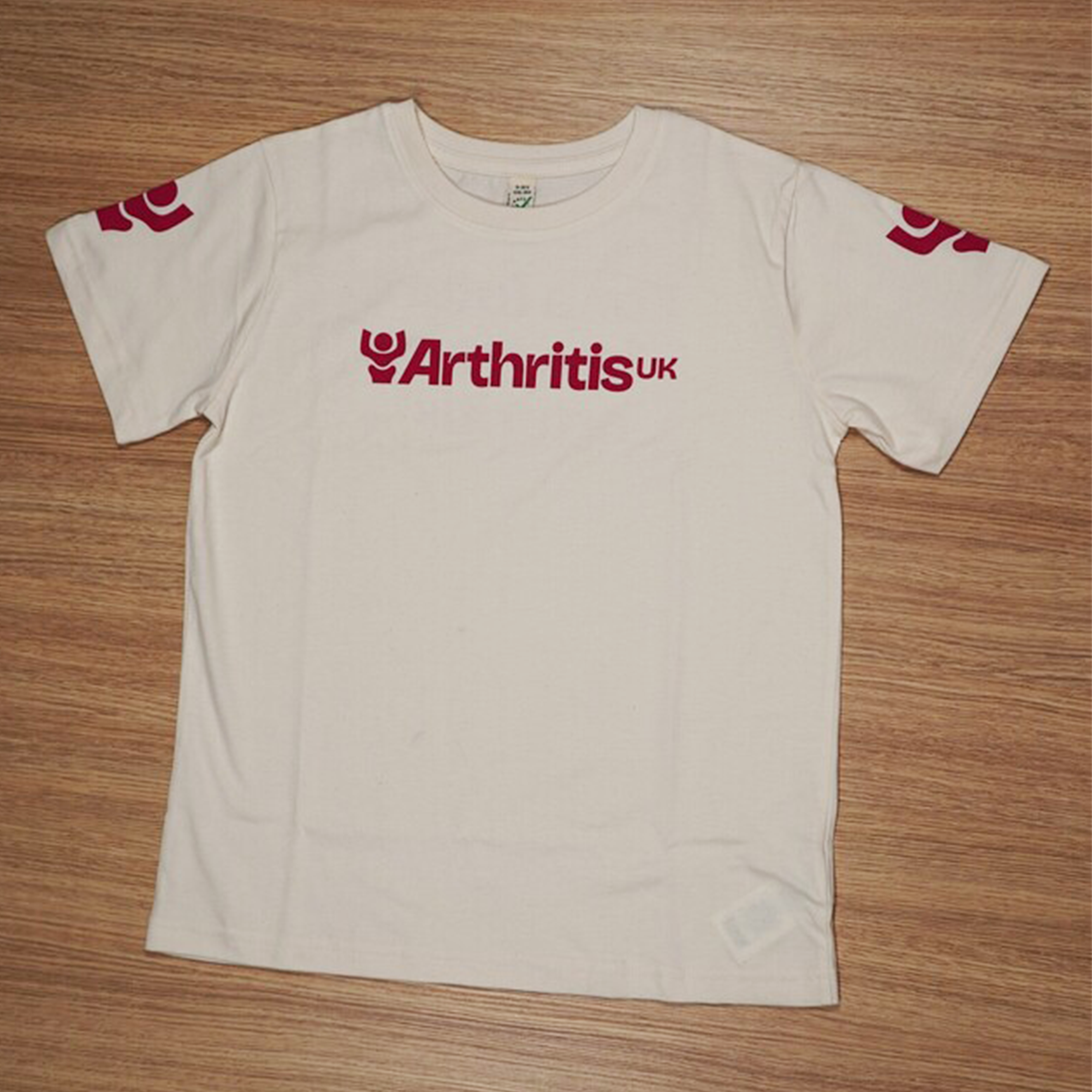 Off White t-shirt with 'Arthritis UK' logo on a wooden surface