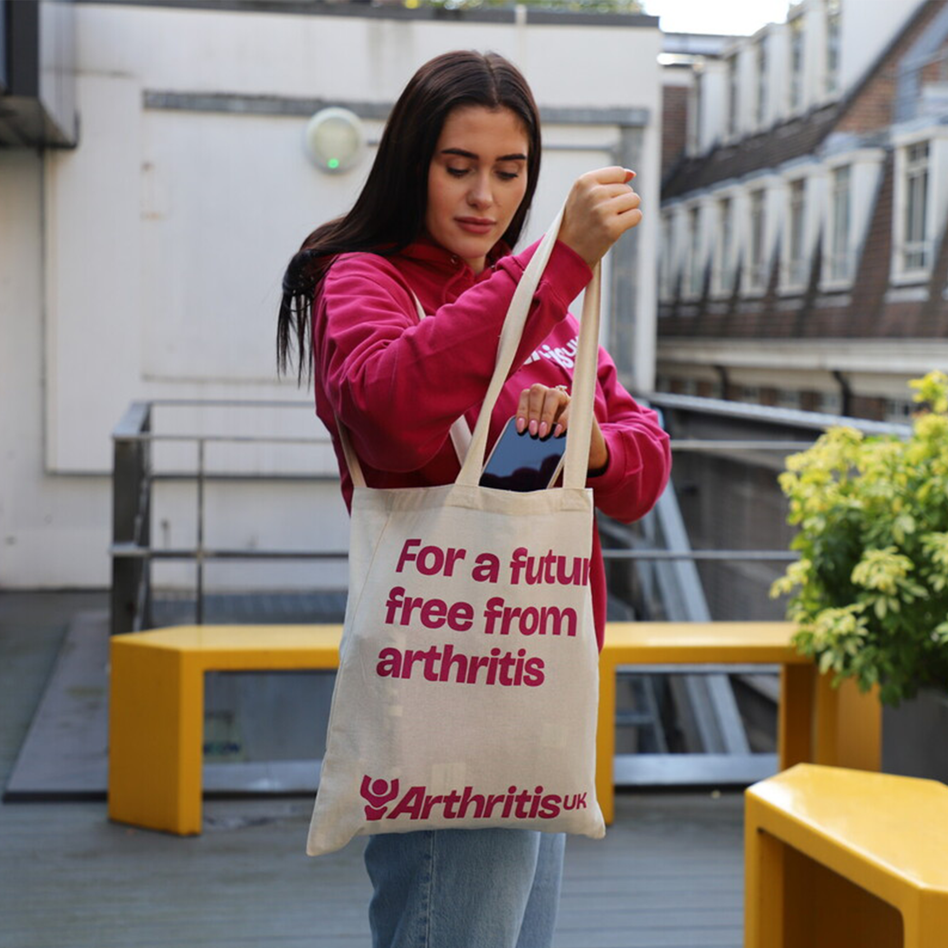 Person holding Arthritis UK tote bag, reading showing logo and 'For a future free from arthritis'.