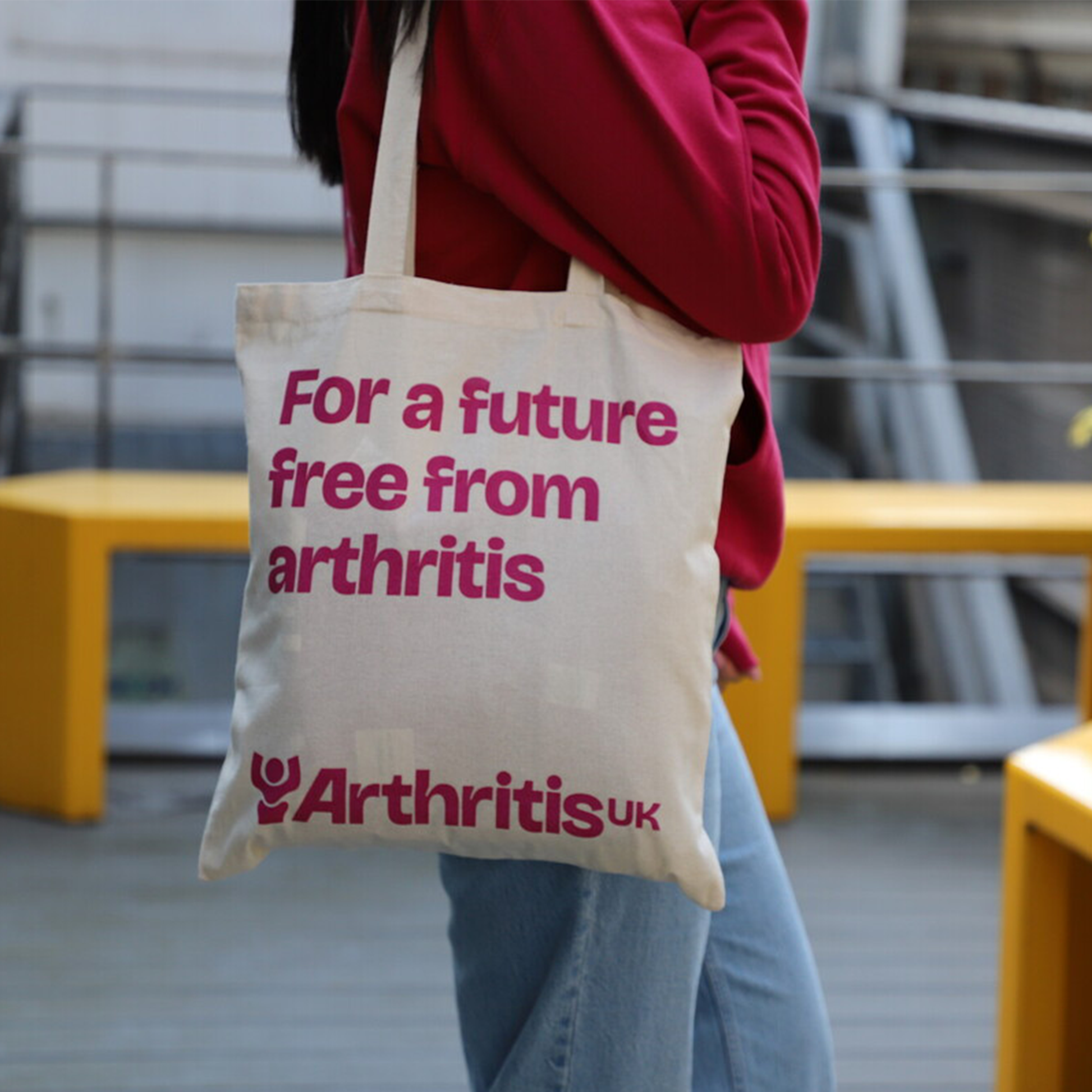 Person holding Arthritis UK tote bag, reading showing logo and 'For a future free from arthritis'.