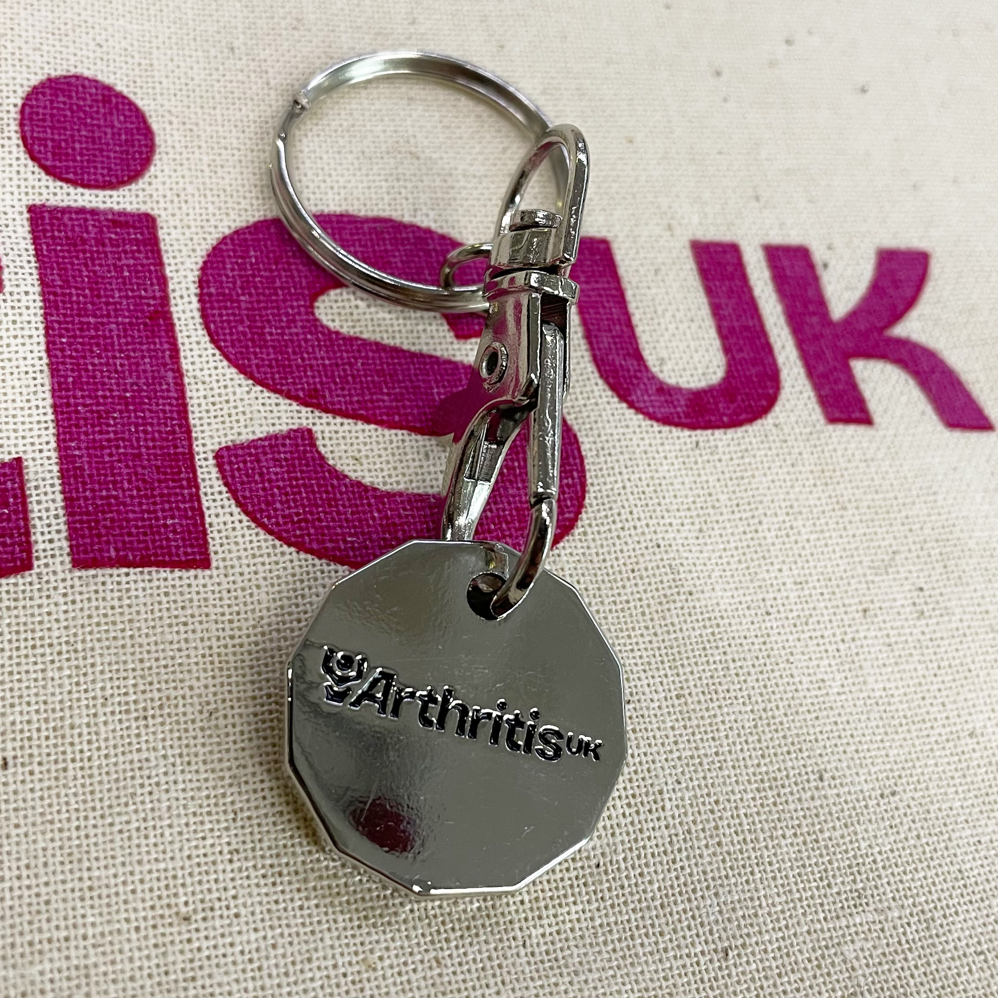 Silver keychain with Arthritis UK logo on a fabric background