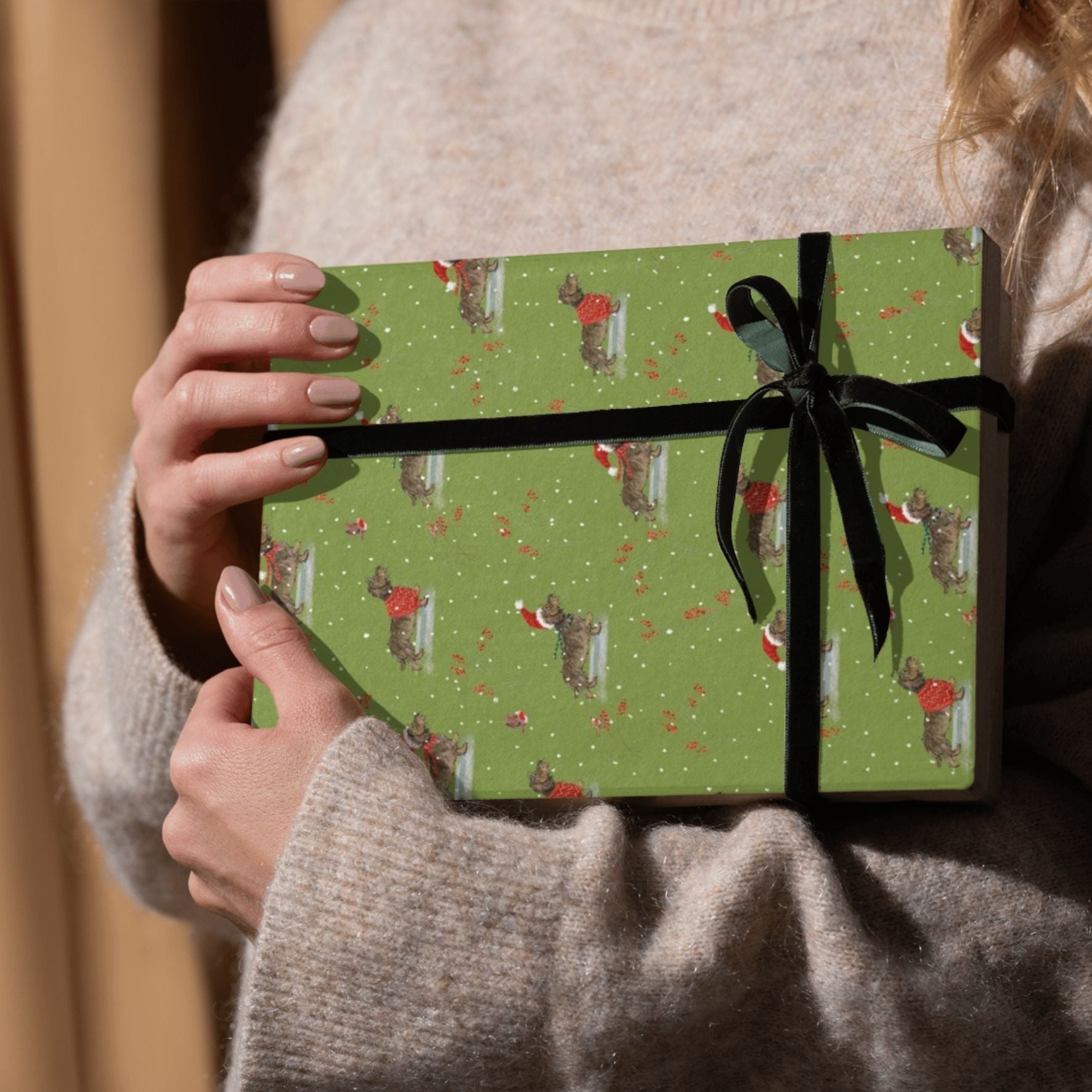 Person holding a green gift box with a black ribbon and festive dogs pattern.