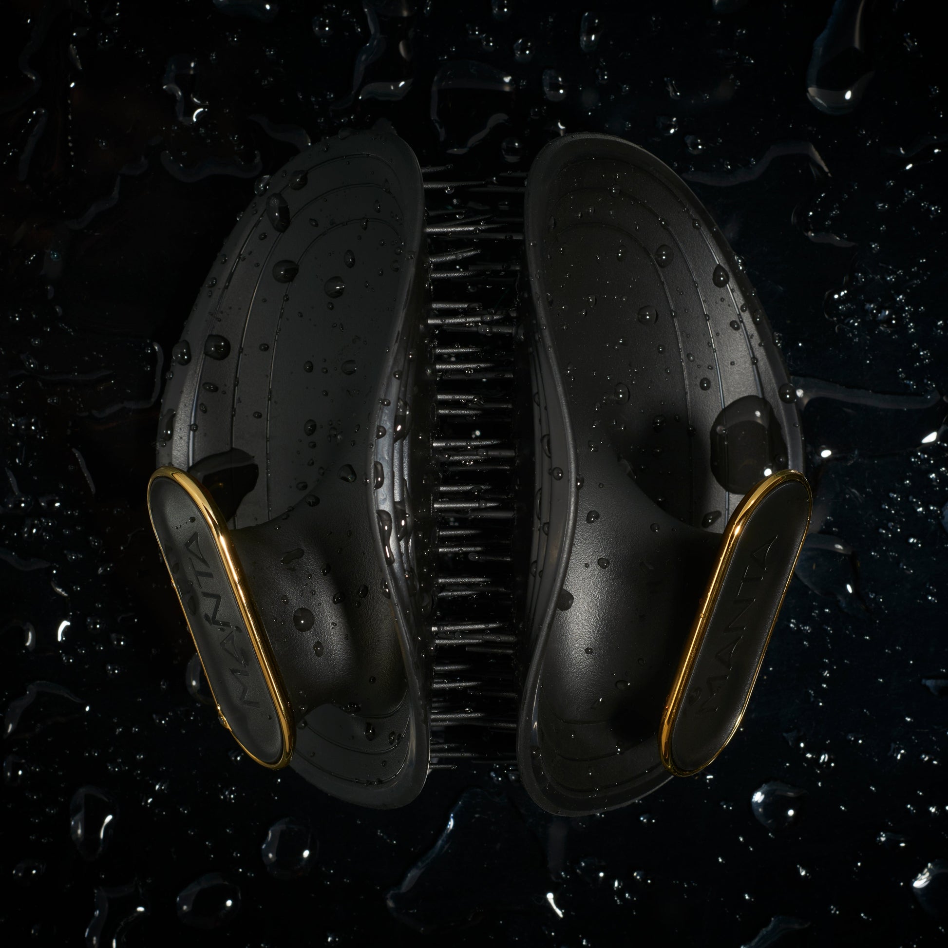 MANTA Black and gold hairbrush on a dark surface with water droplets