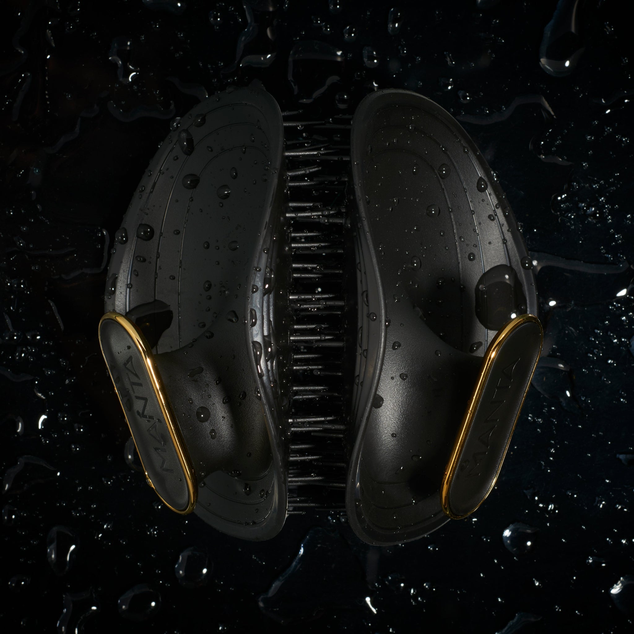 MANTA Black and gold hairbrush on a dark surface with water droplets