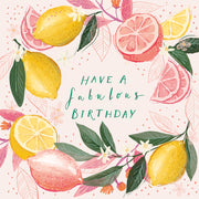 A square birthday card design featuring watercolor-style lemons, pink grapefruit slices, green leaves, and small white flowers arranged around the text 'HAVE A fabulous BIRTHDAY' in teal script on a pale pink background with subtle polka dots.