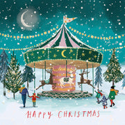 Front cover of the Arthritis UK Christmas Card 'Christmas Carousel' featuring a festive fairground ride in a snowy landscape, with the text 'Happy Christmas'. 