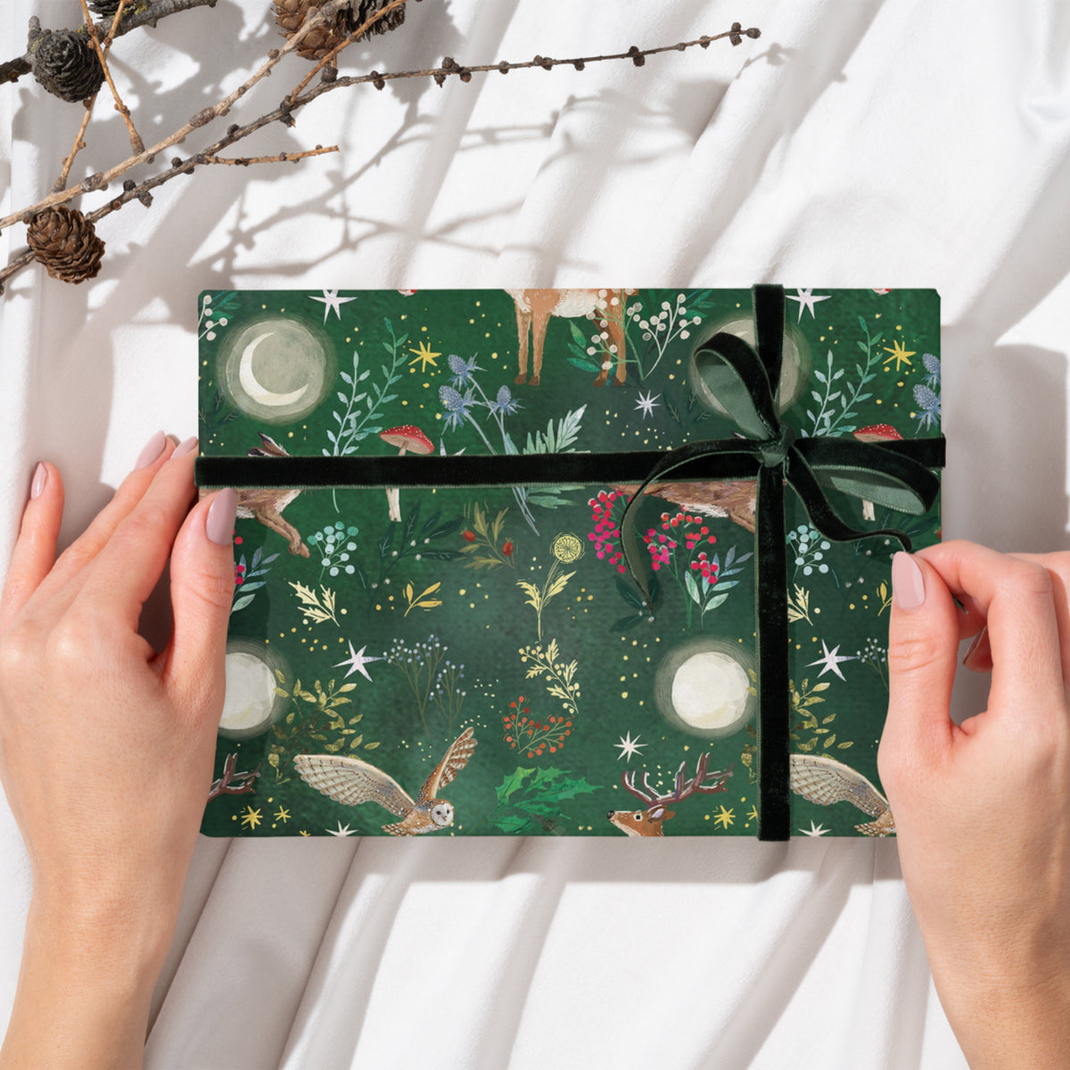 Gift wrap featuring deer, owls, hares and foliage against a green moonlit background.  