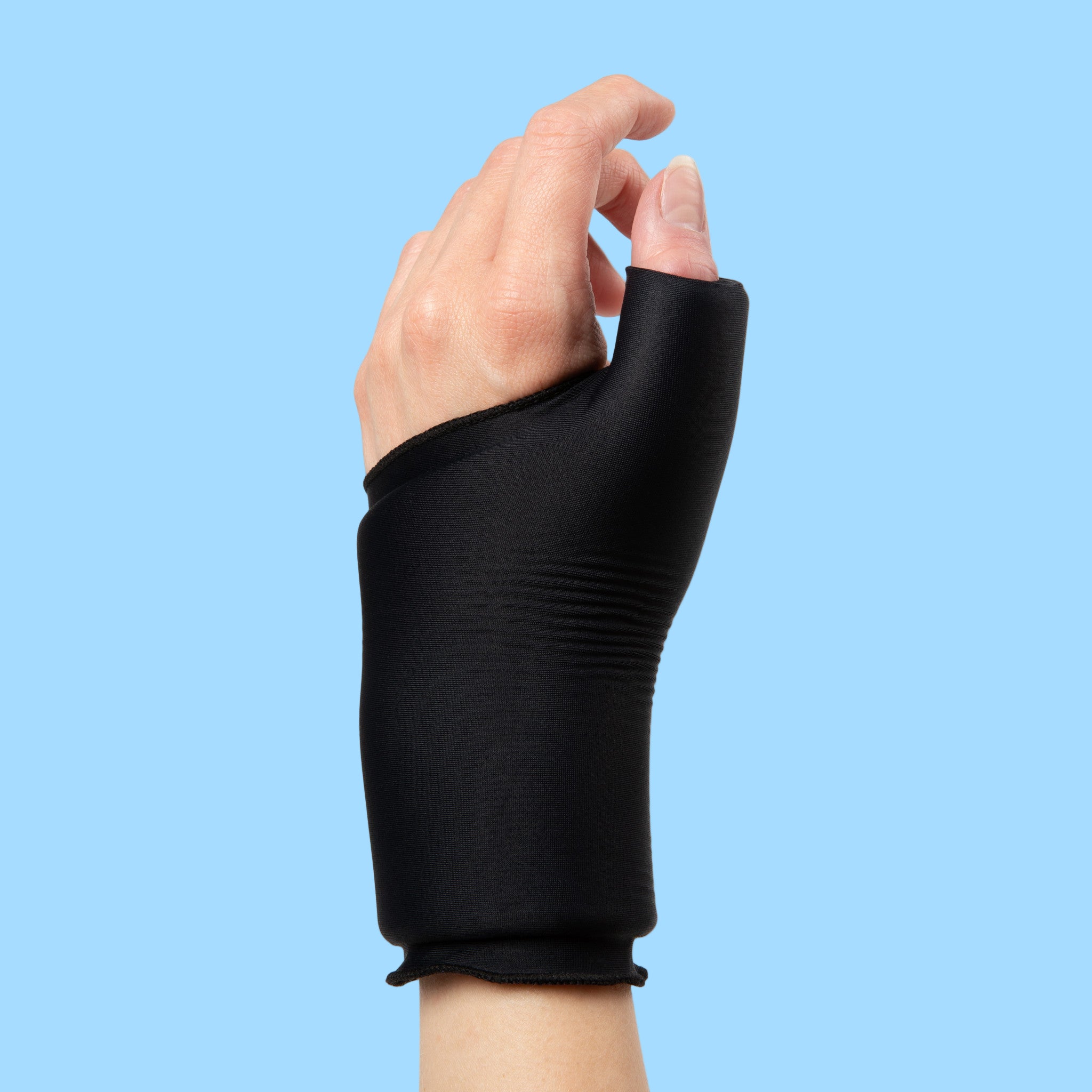 Hand wearing a blackGrace and Able Cooling Compression Sleeve For Thumb & Wrist Pain on a blue background.