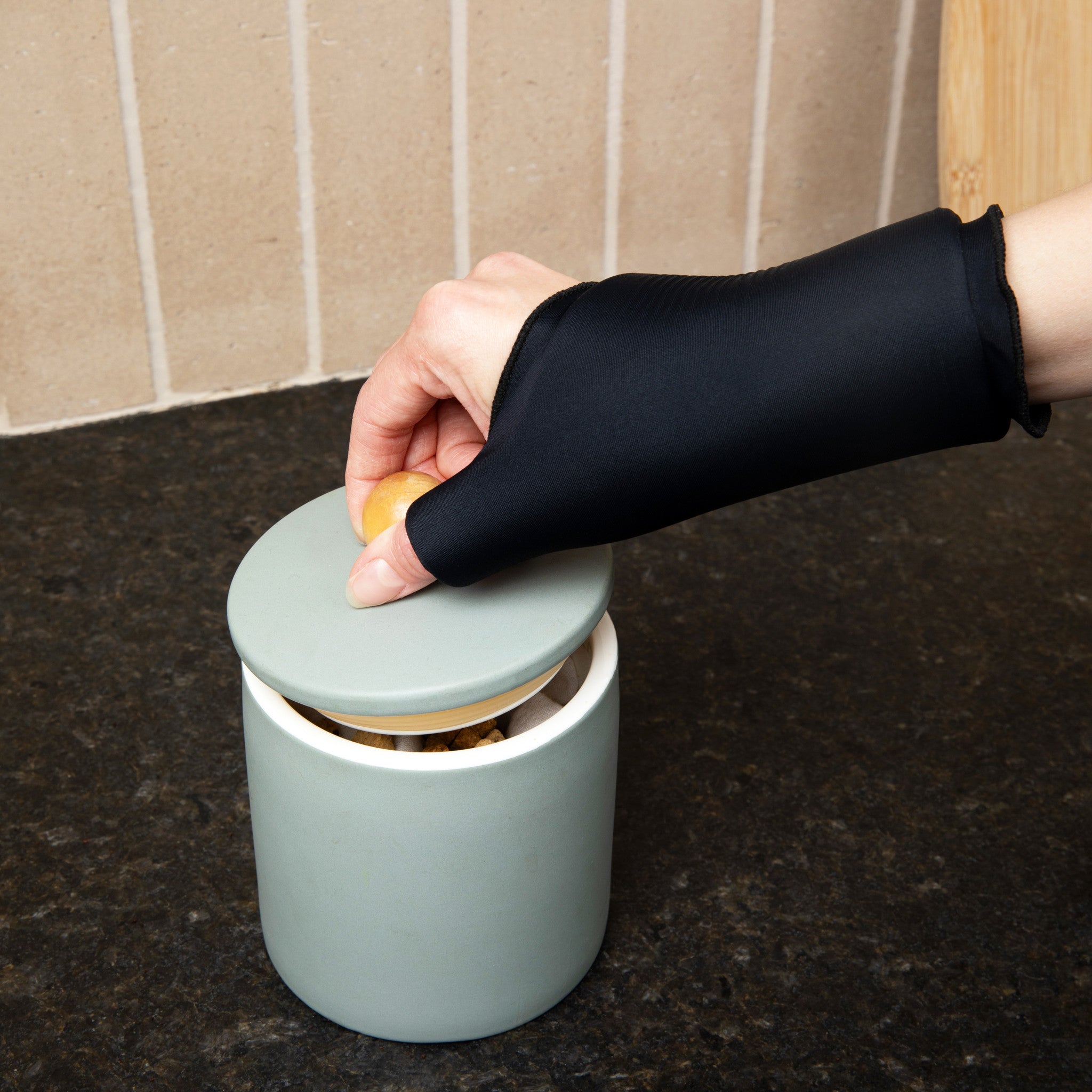 Person opening a jar wearing the Grace and Able Cooling Compression Sleeve For Thumb & Wrist Pain in black. 