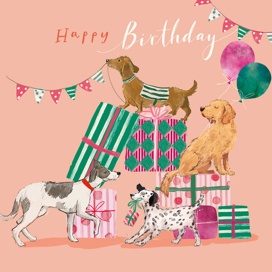 An illustrated birthday scene with three dogs among wrapped presents and balloons on a peach background, with the words 'Happy Birthday' at the top.
