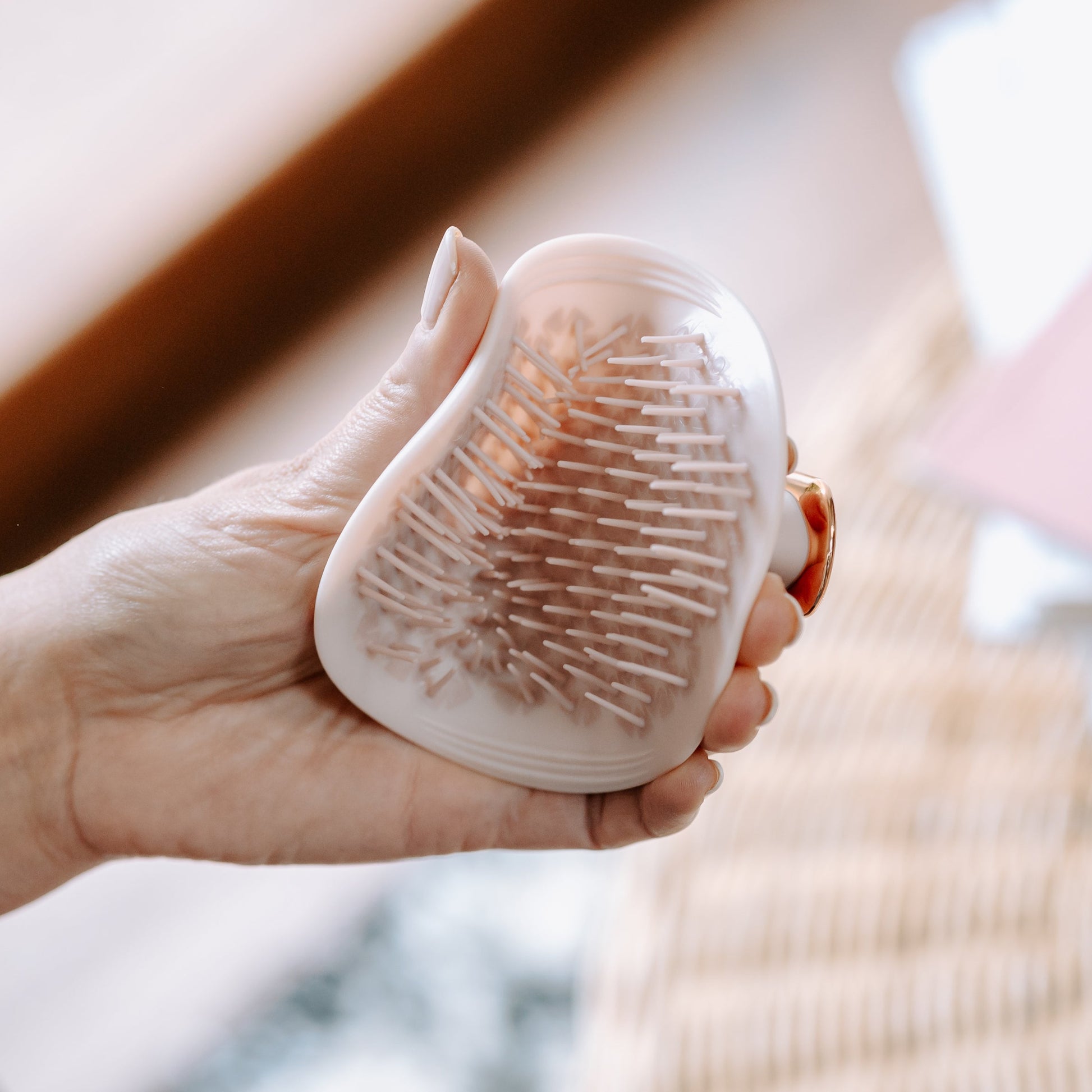 MANTA detangling brush in pink and rose gold, held in a hand.