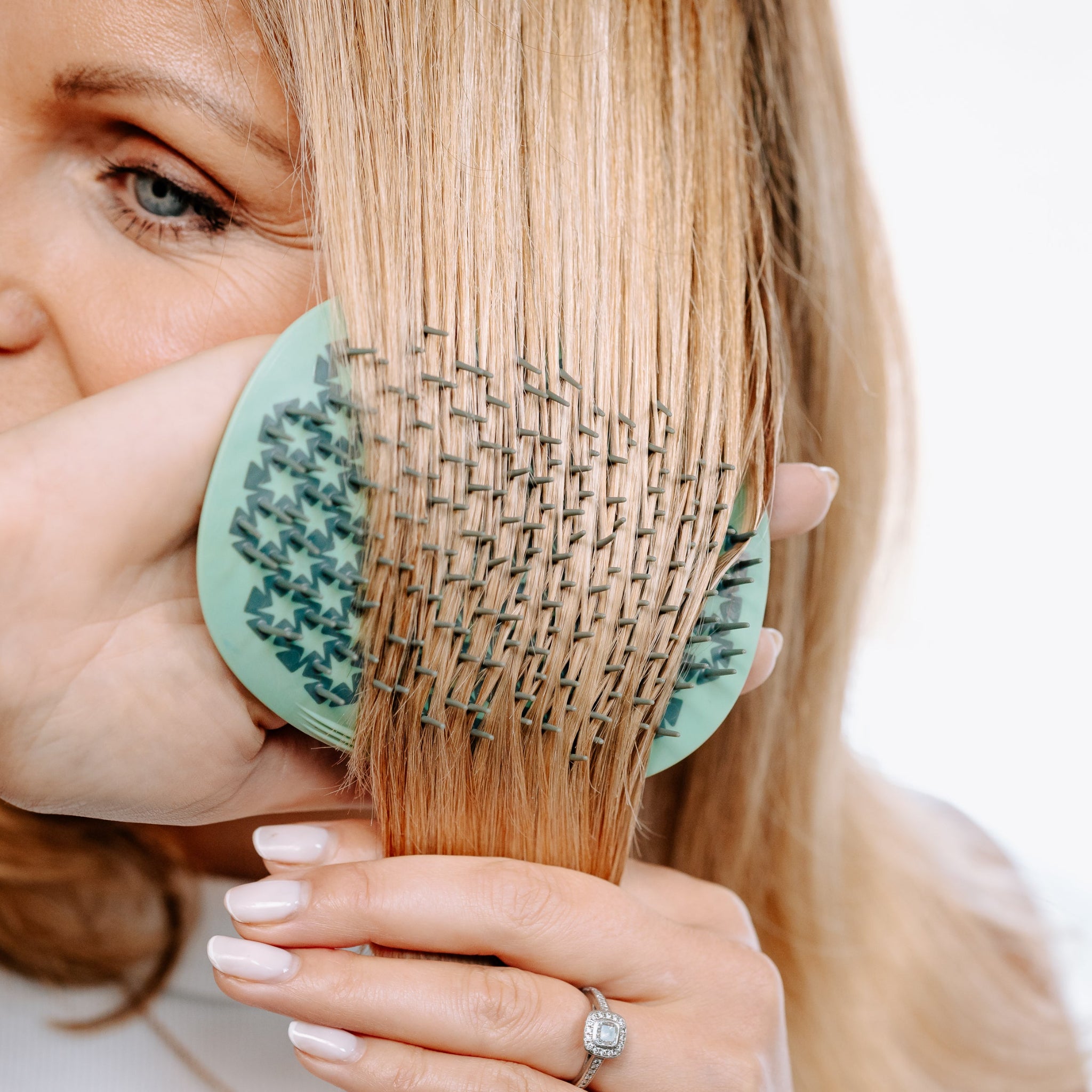 Woman using the MANTA detangling brush in green and white gold to brush her hair. 