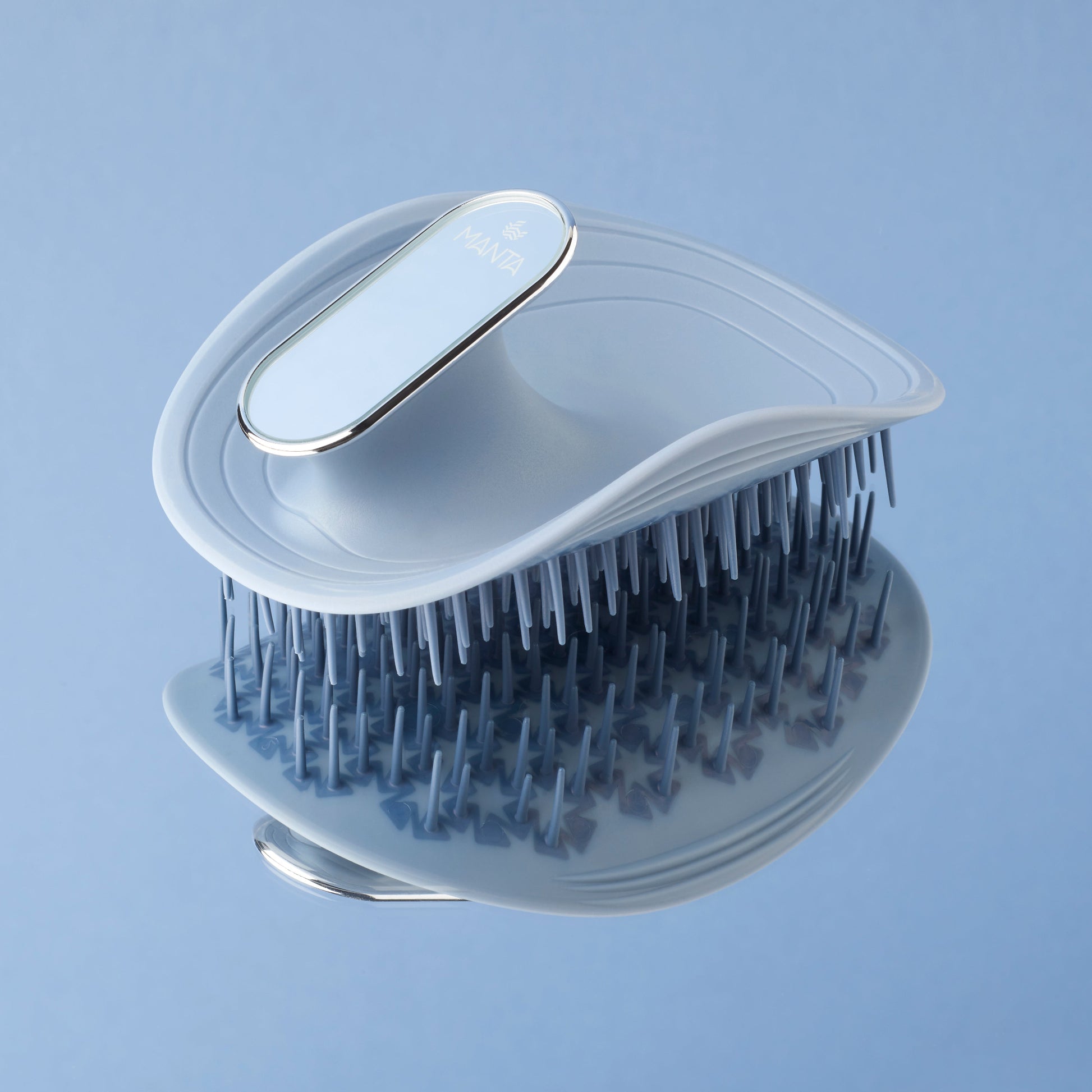 MANTA mirror travel brush with a non-slip handle in blue and white gold on a mirrored surface. 