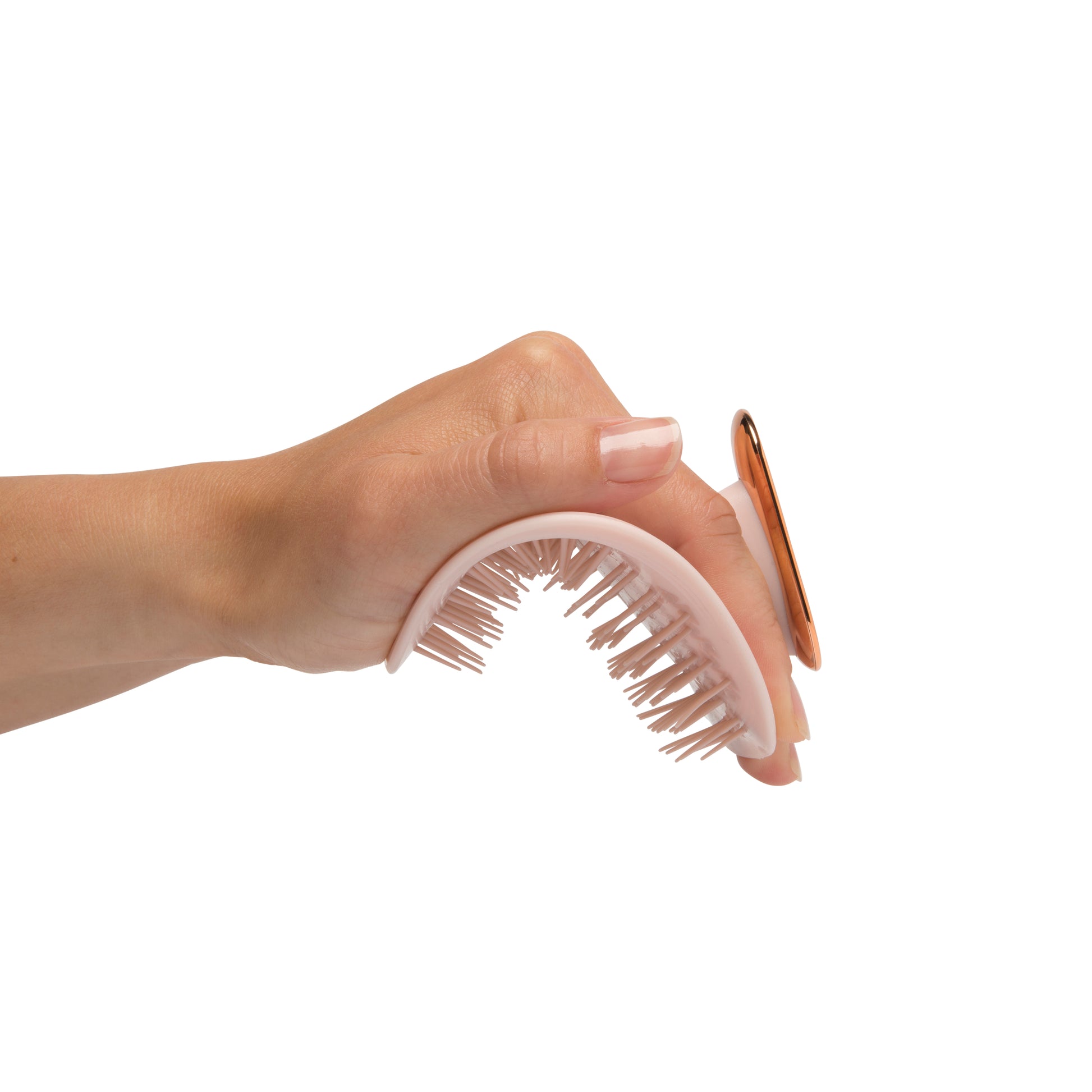 MANTA brush with a non-slip handle in pink and rose gold, being flexed in the palm of a hand. 