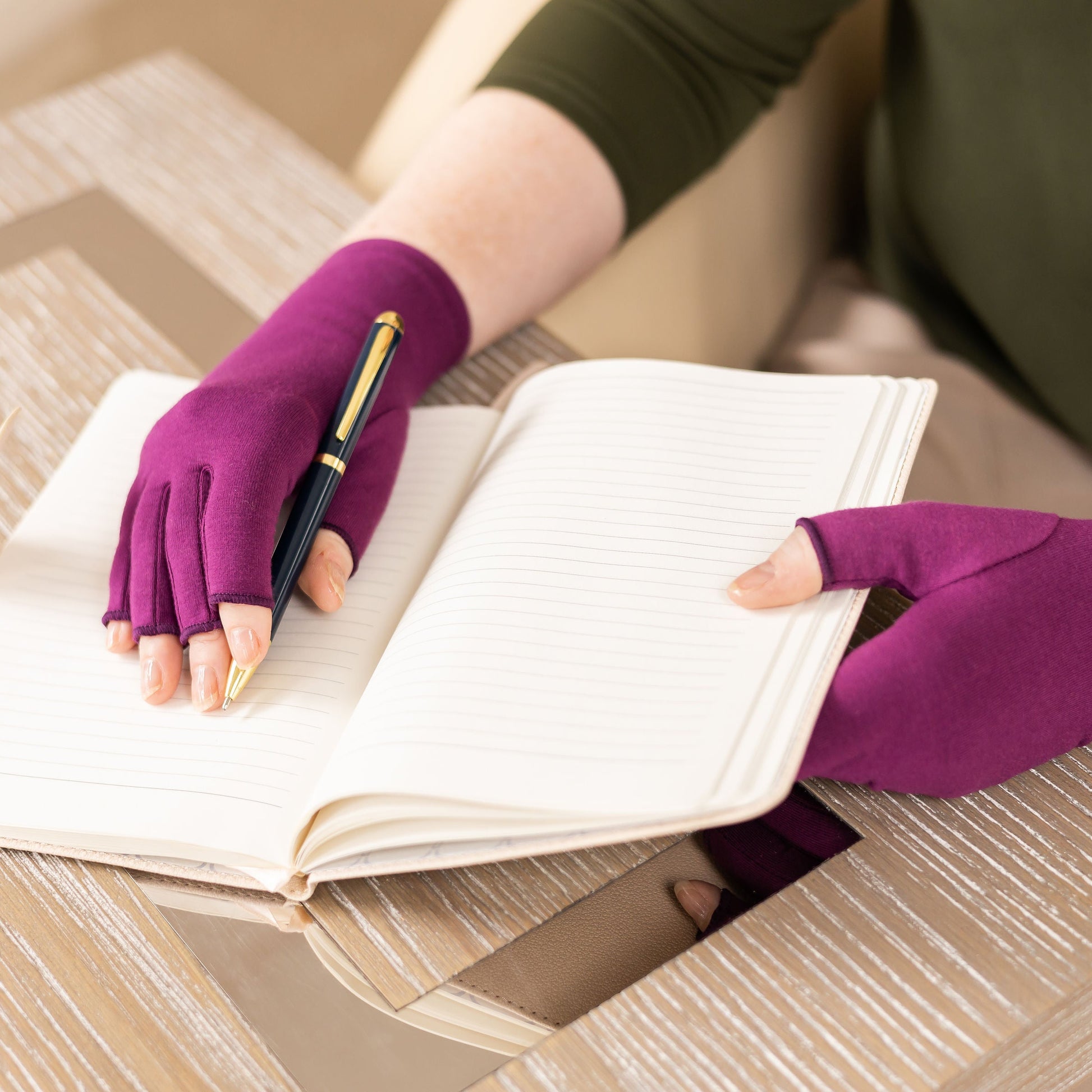Grace and Able unisex compression arthritis gloves for swelling being worn whilst writing in a notebook, in plum purple. 