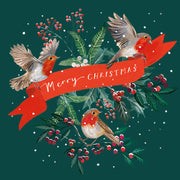 Front cover of the Arthritis UK Christmas Card 'Red Ribbon' featuring three robins holding up a red ribbon, in front of winter leaves. The red ribbon reads 'Merry Christmas'. 