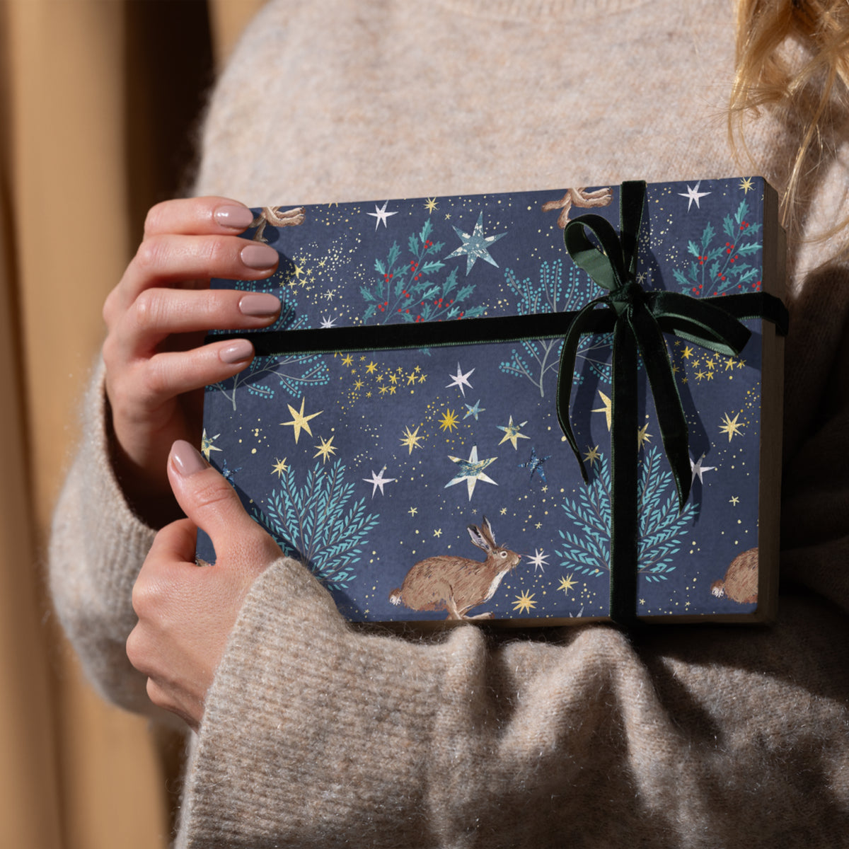 Gift wrap featuring hares and winter foliage against a starlit sky. 