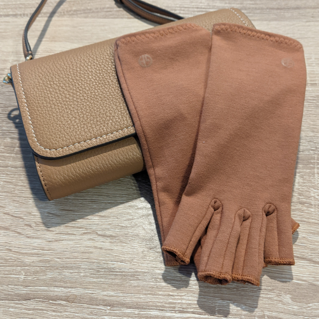Grace and Able skin tones compression gloves in caramel brown next to a beige handbag. 