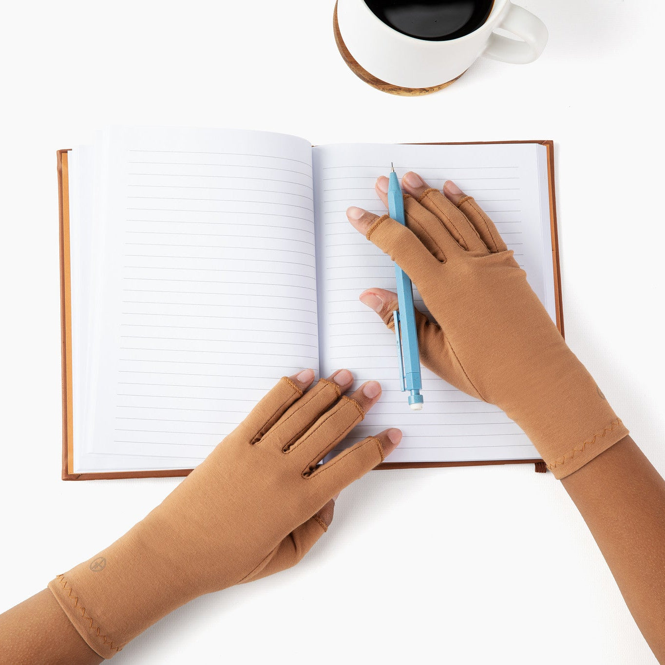 Hands wearing cinnamon brown compression gloves holding open a notebook and mechanical pencil
