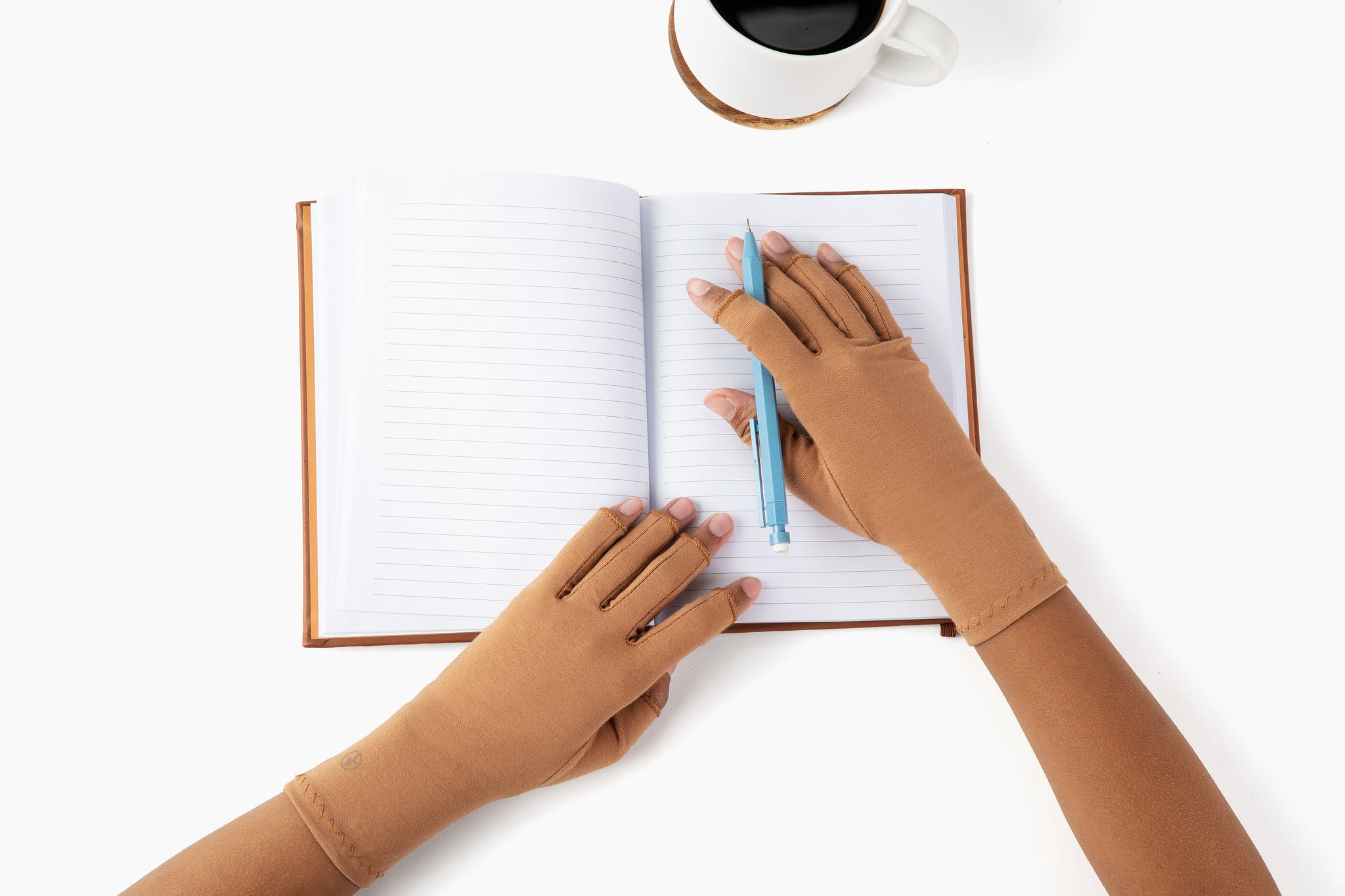 Hands wearing cinnamon brown compression gloves holding open a notebook and mechanical pencil