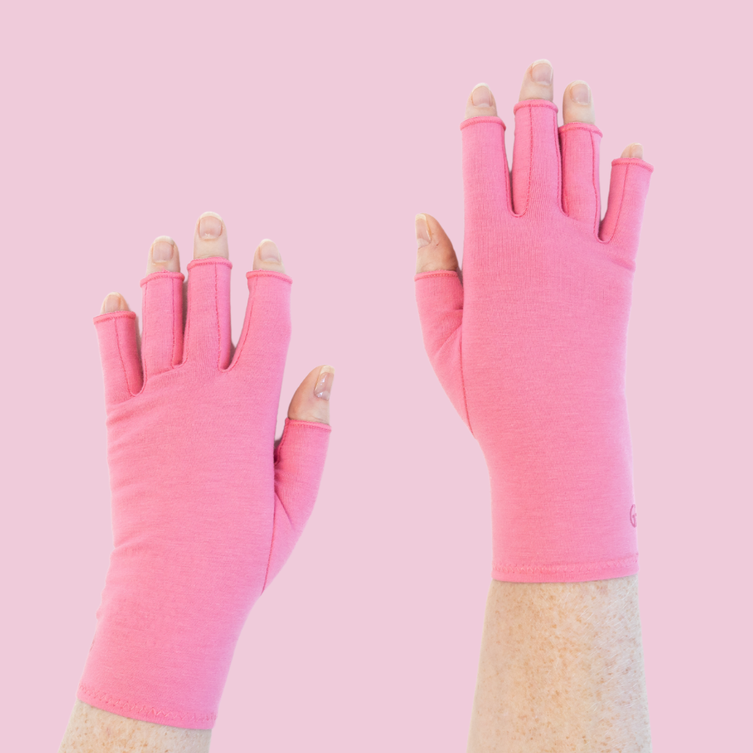 A pair of pink compression gloves designed to alleviate joint pain, with the hands facing forward showing the palm side of the gloves.