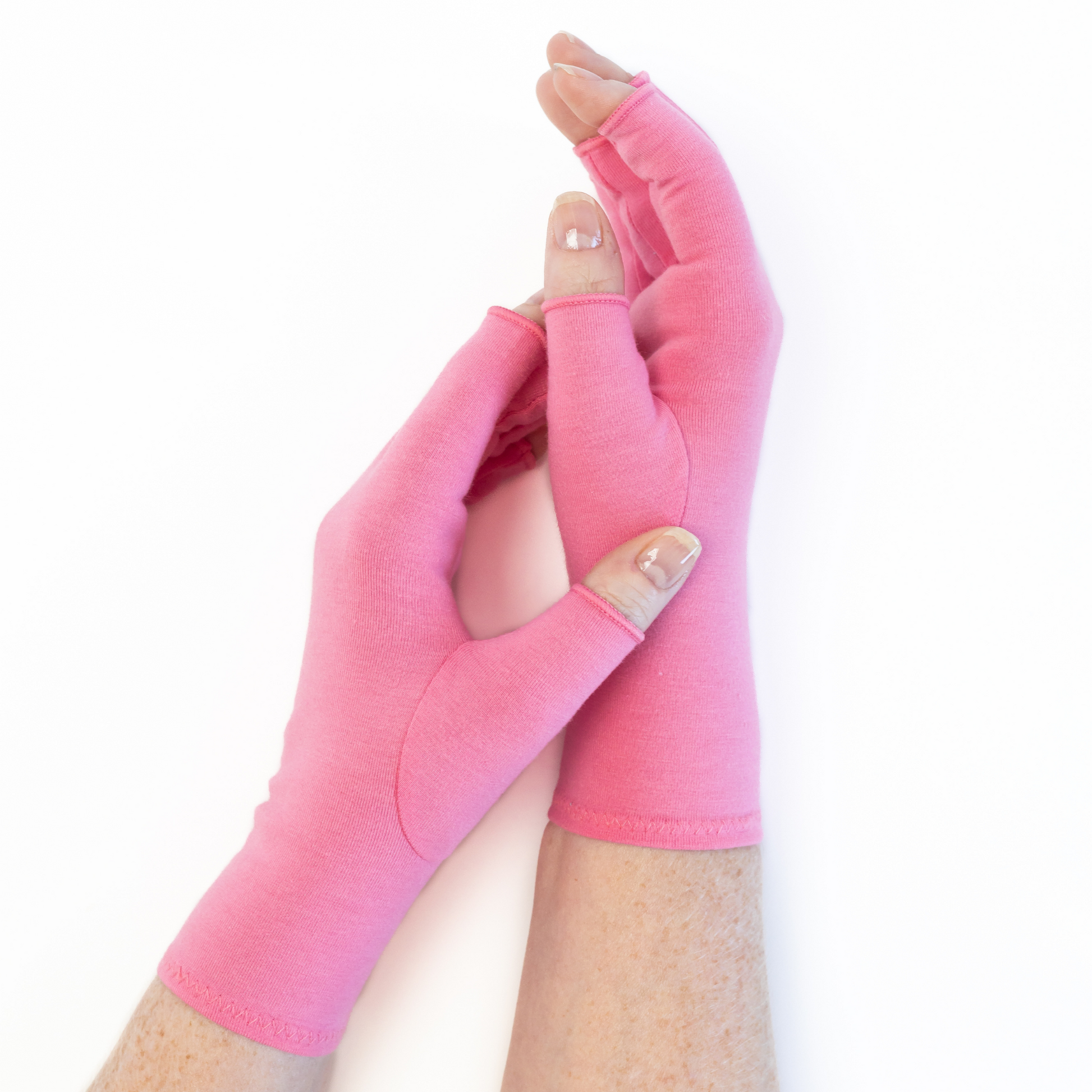 A pair of Grace and Able unisex arthritis compression gloves in coral pink, shown being worn. 