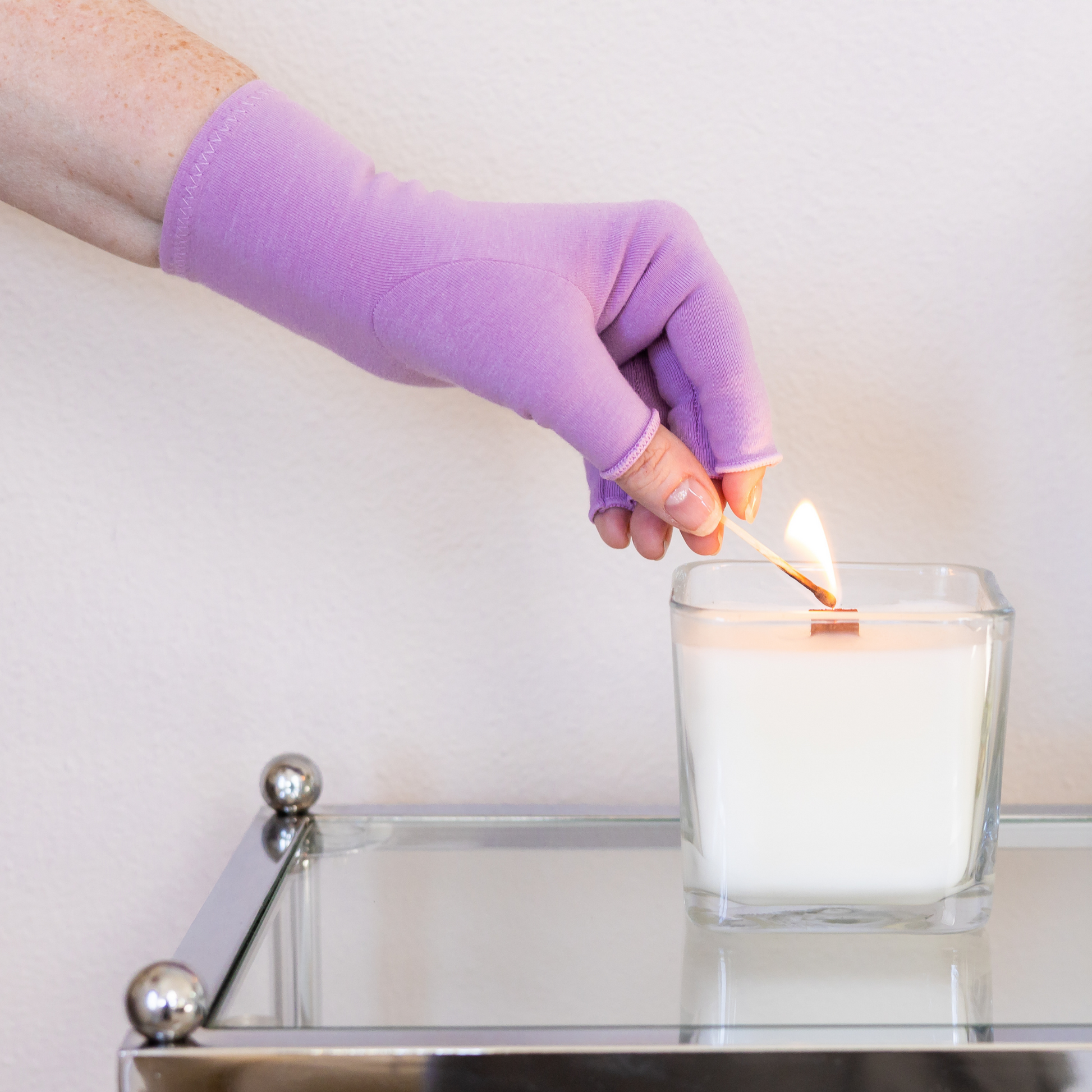 Grace and Able arthritis compression gloves in purple, shown on a hand lighting a candle. 
