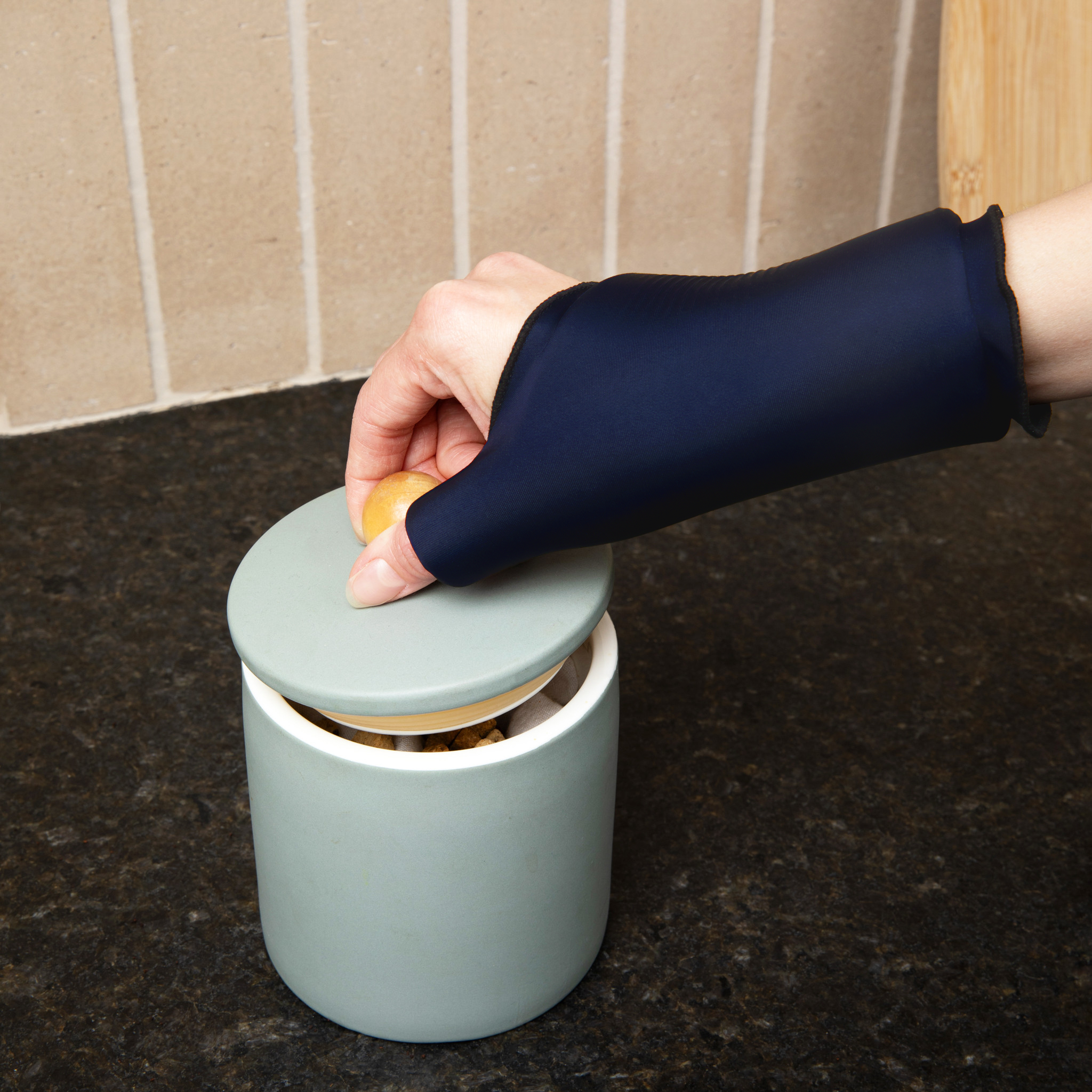 Person wearing a Grace and Able Cooling Compression Sleeve For Thumb & Wrist Pain in midnight blue opening a jar. 