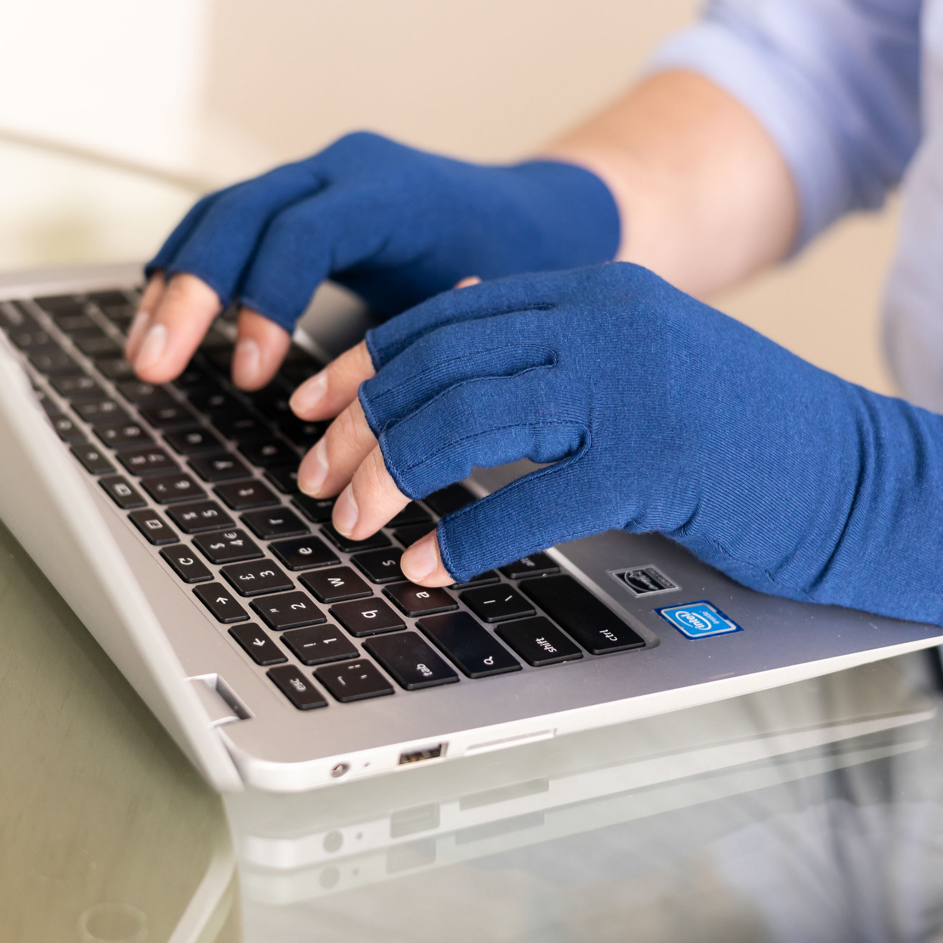 Best arthritis compression gloves for men and women, in marine blue, shown being worn whilst typing on a laptop. 