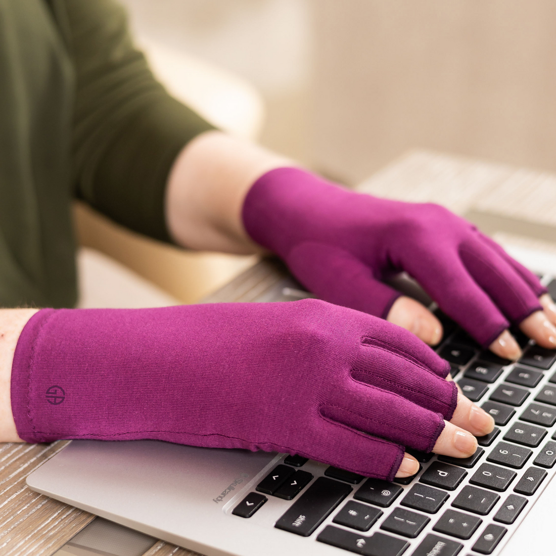 Therapeutic compression gloves in plum purple shown being worn whilst typing on a laptop. 