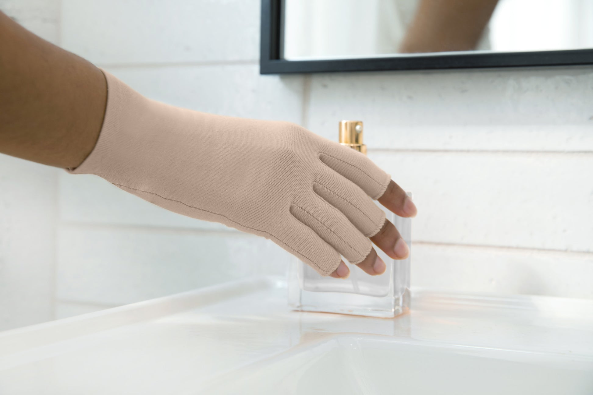 hand wearing sandy beige compression glove holding a perfume bottle